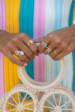 Model wearing gold statement stacking rings featuring pink, aquamarine, and white cz stones. 