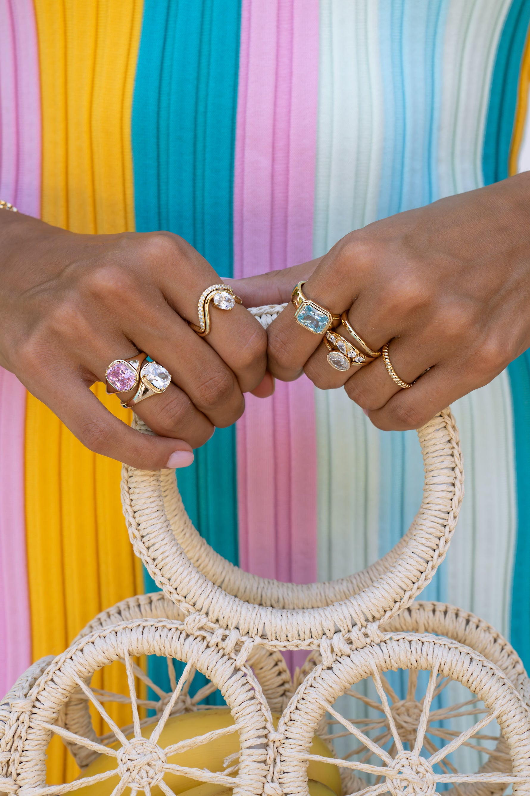 Model wearing gold statement stacking rings featuring pink, aquamarine, and white cz stones. 