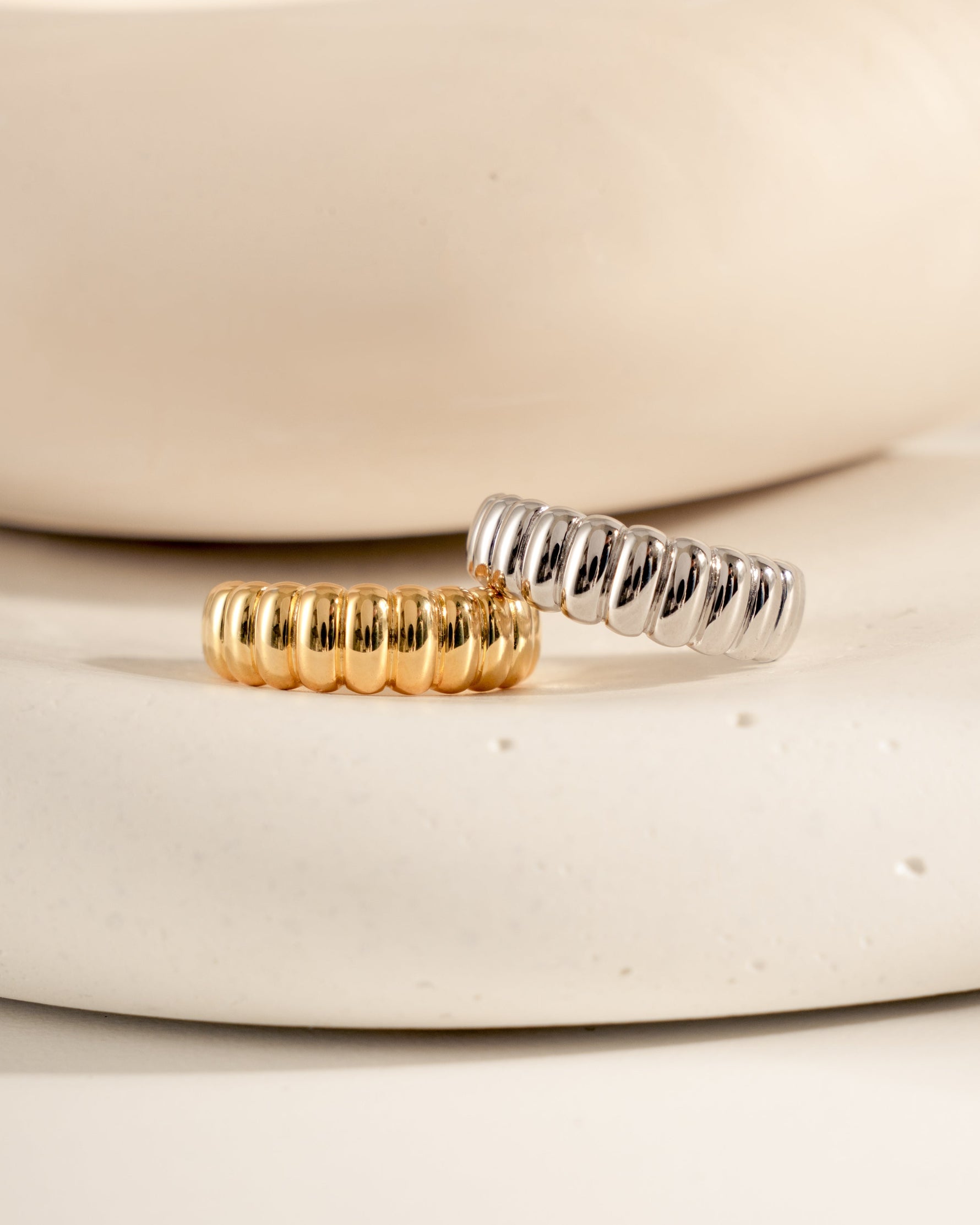Chunky fluted statement rings in both gold and silver on a textured surface.
