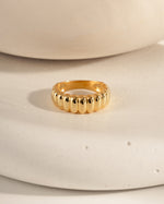 Chunky gold fluted statement ring on a textured surface.