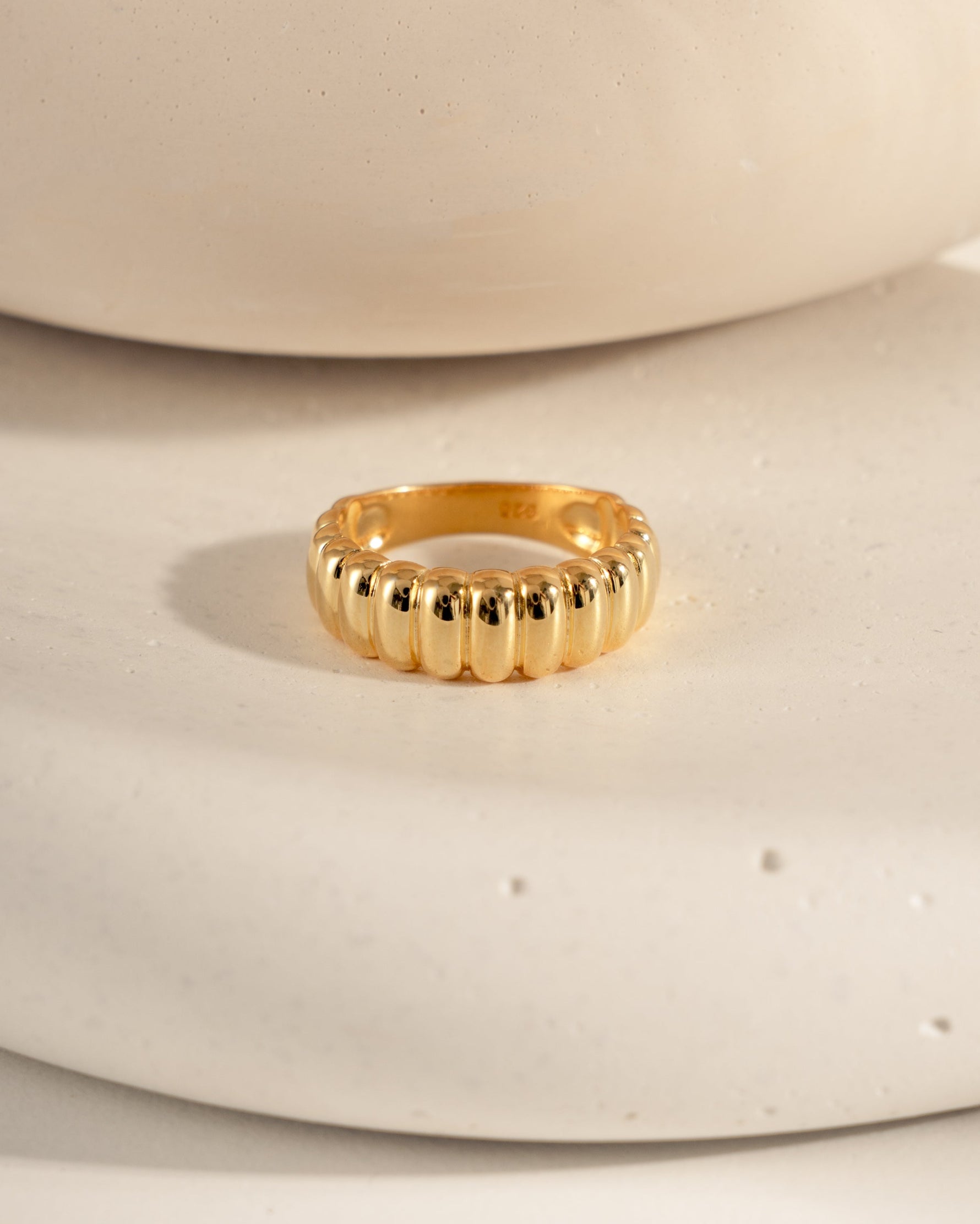 Chunky gold fluted statement ring on a textured surface.