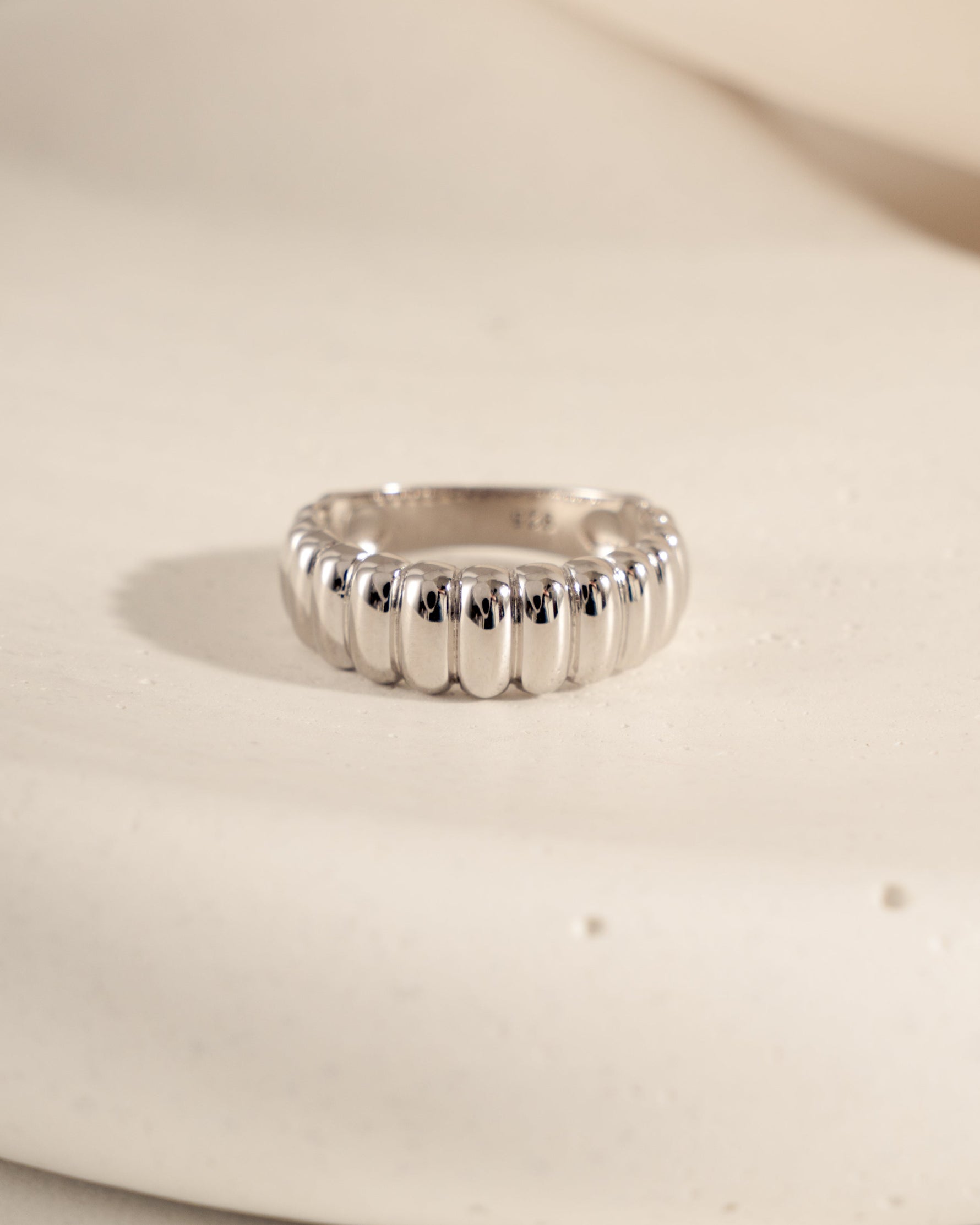Chunky sterling silver fluted statement ring on a textured surface.