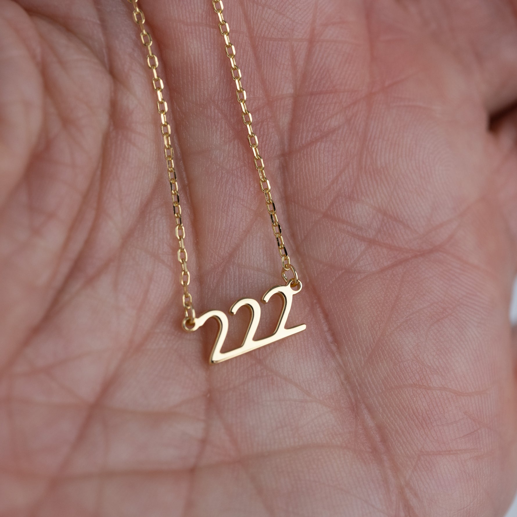Model holding gold 222 lucky angel number necklace in hand