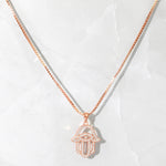 Rose gold hamsa necklace with cz stones on marble background. 