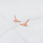 Rose gold studded lightning bolt stud earrings on marble background.
