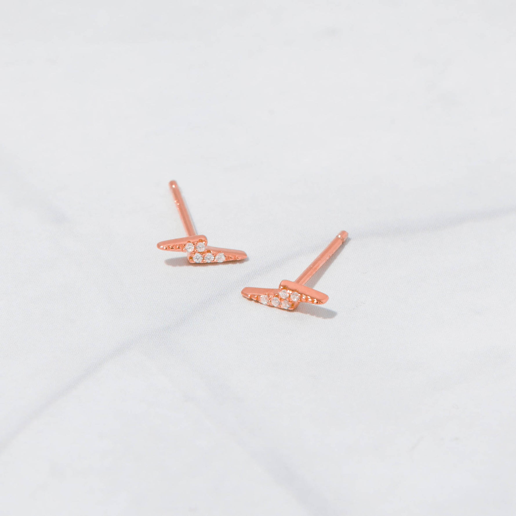 Rose gold studded lightning bolt stud earrings on marble background.