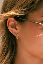Model wearing gold aquamarine baguette stud earrings paired with multi-stone gold huggie earrings. 