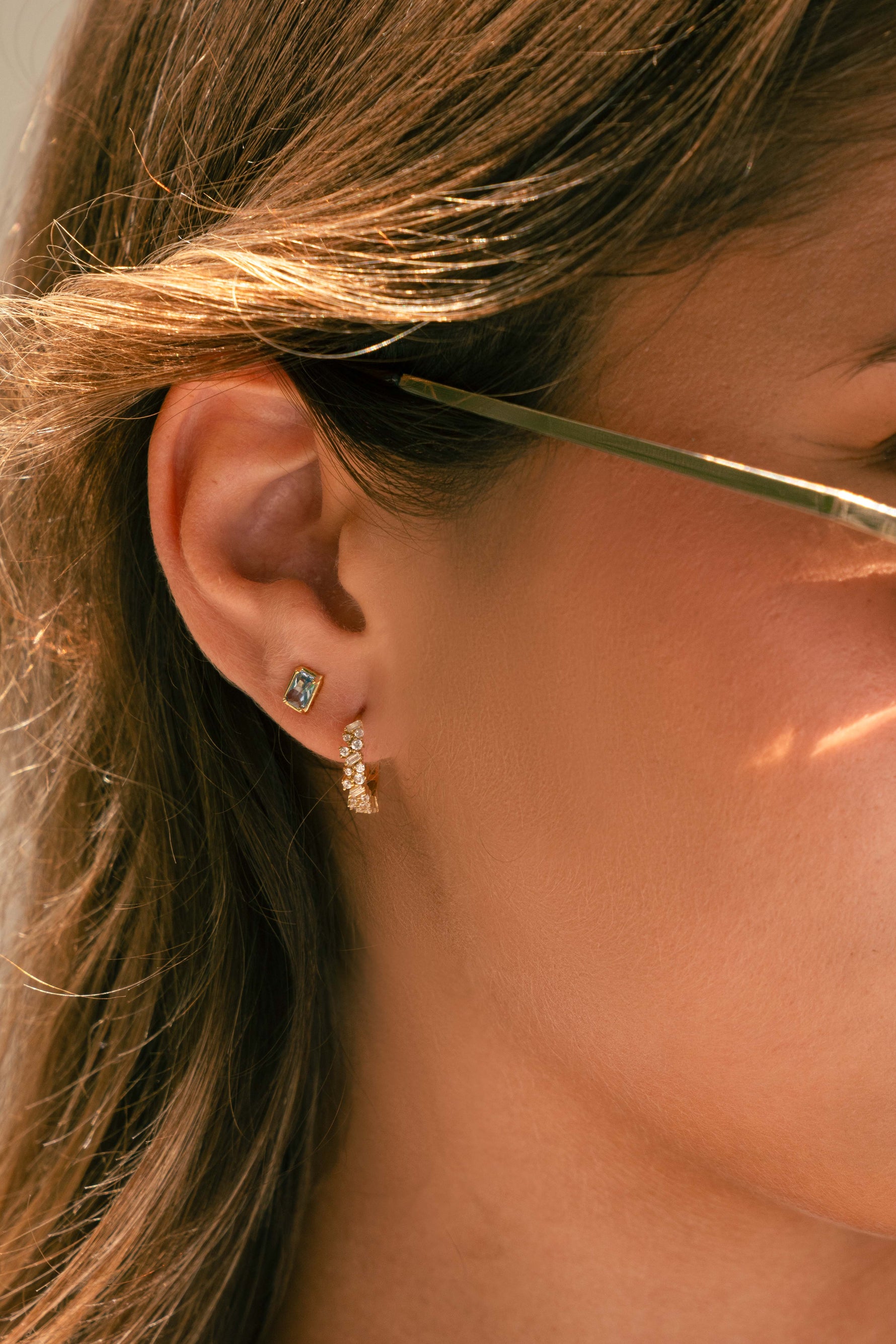 Model wearing gold aquamarine baguette stud earrings paired with multi-stone gold huggie earrings. 