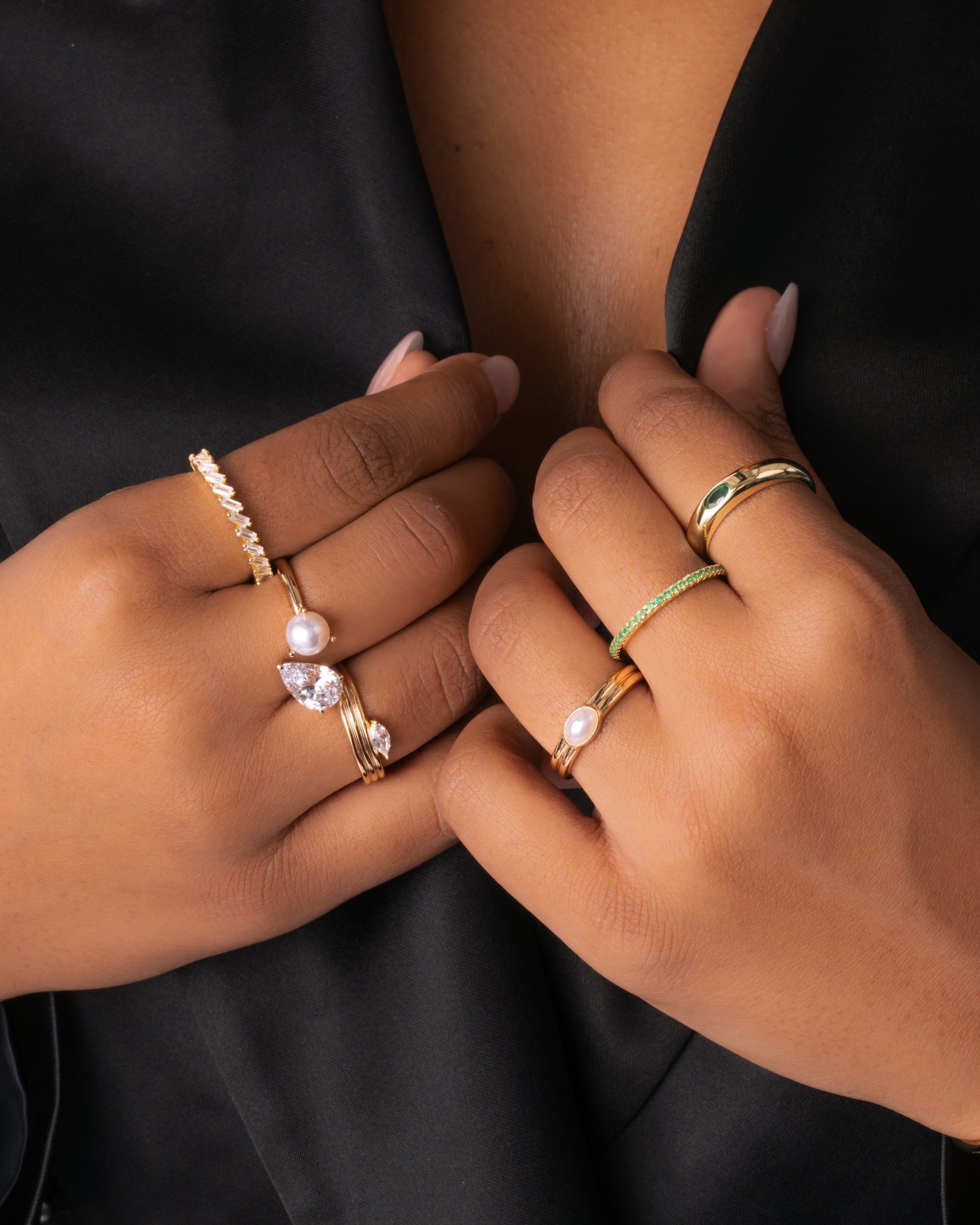 Model wearing bold statement gold rings including emerald and pearl stones. 