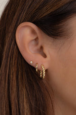 Model wearing gold twisted hoop earrings paired with simple huggies and a diamond stud. 