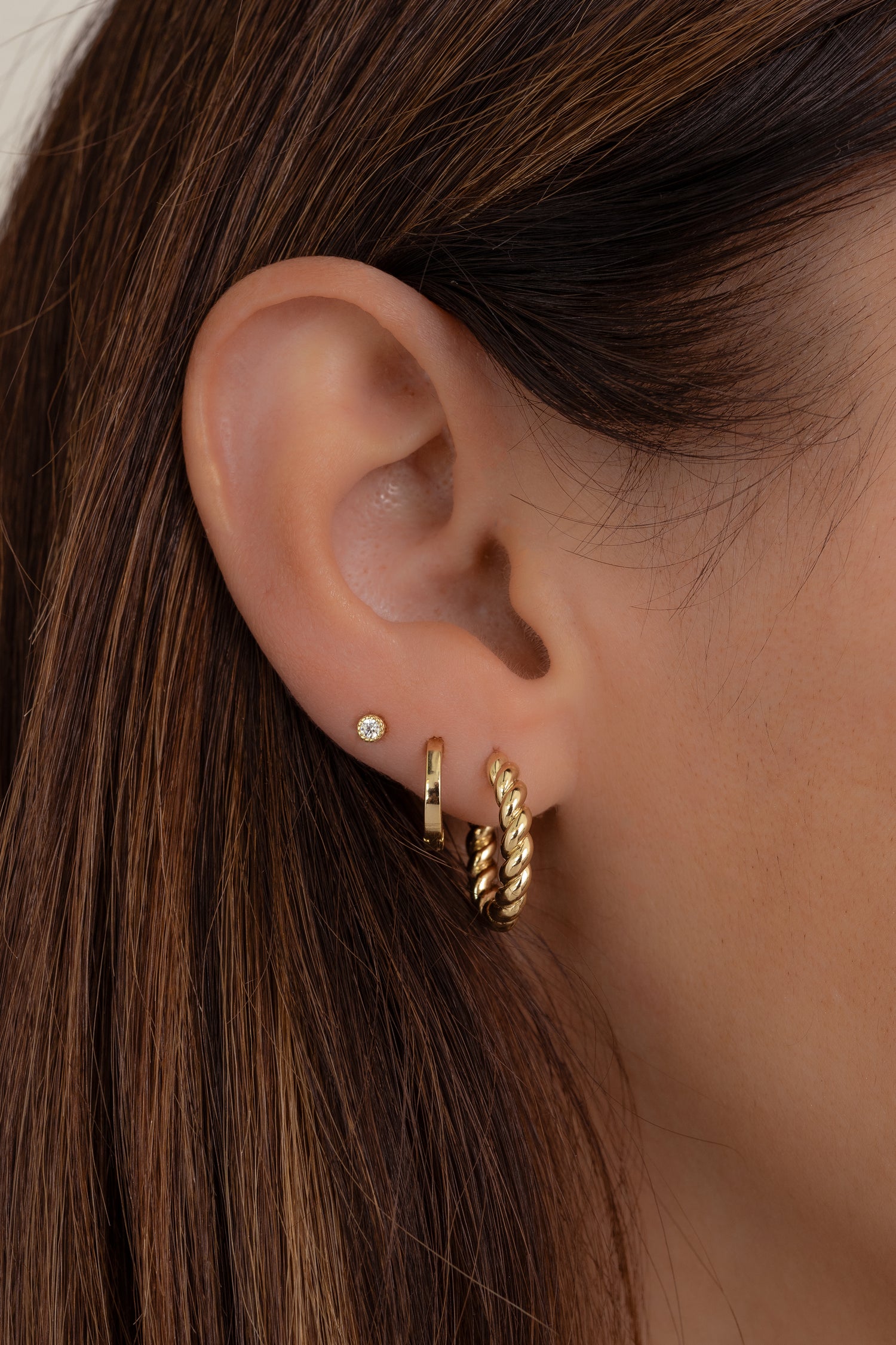 Model wearing gold twisted hoop earrings paired with simple huggies and a diamond stud. 