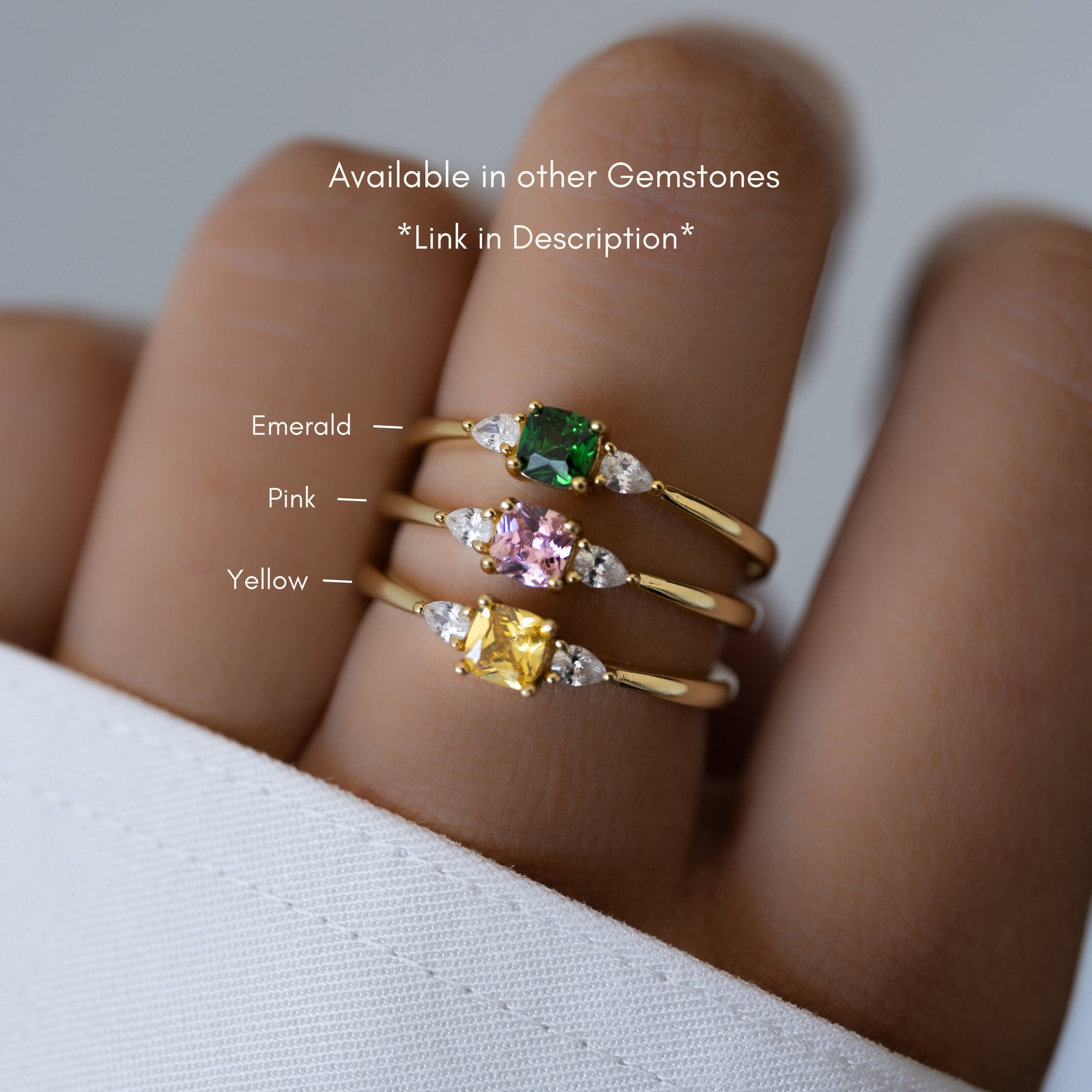 Model wearing gold birthstone rings in emerald, pink, and yellow. 