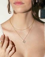 Model wearing delicate gold thin twist chain layered with a mother-of-pearl clover pendant necklace. 