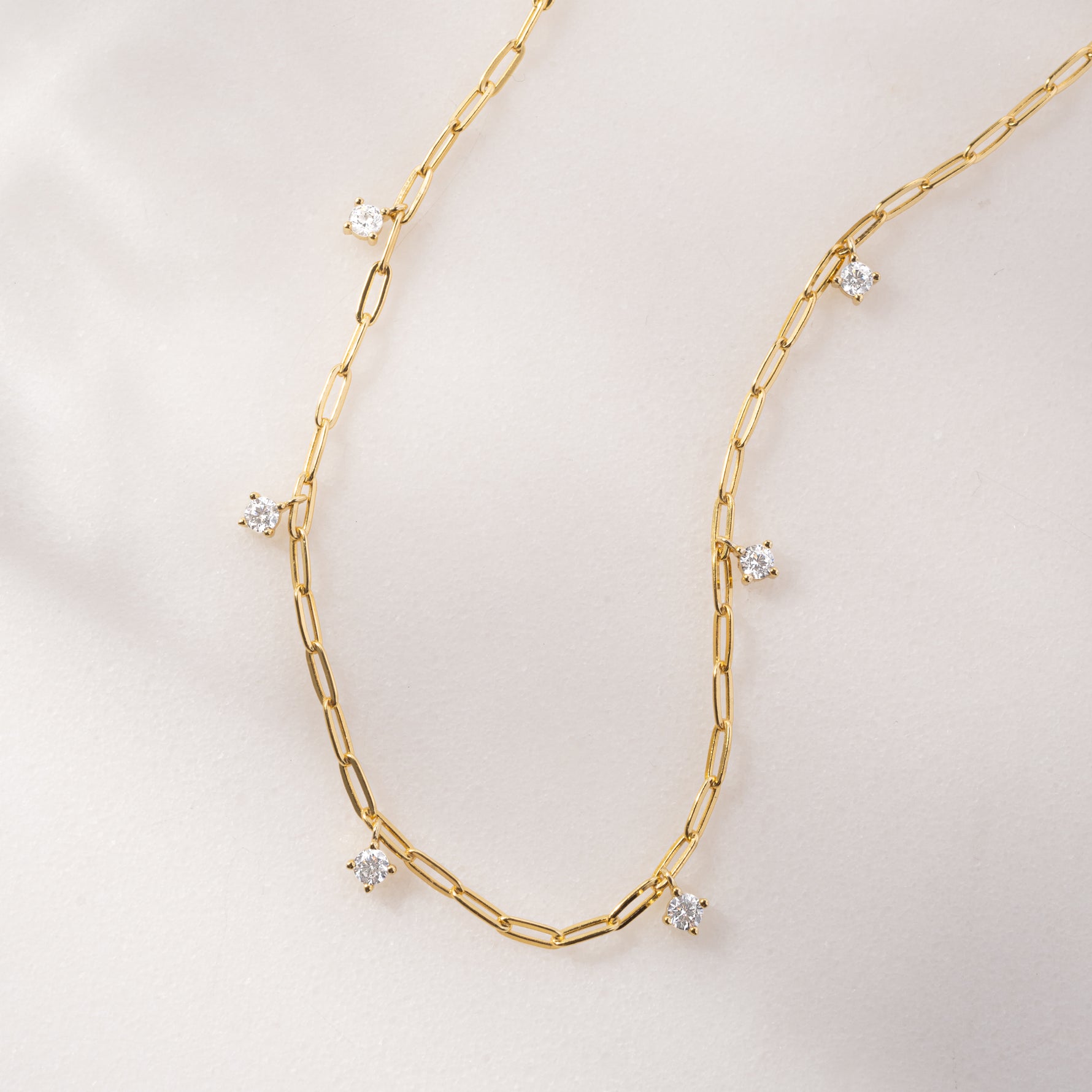 Gold paperclip dainty chain necklace with cz charms on a plain background.