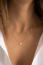 Model wearing dainty gold opal and cz charm necklace and opal oval halo pendant in a stack. 