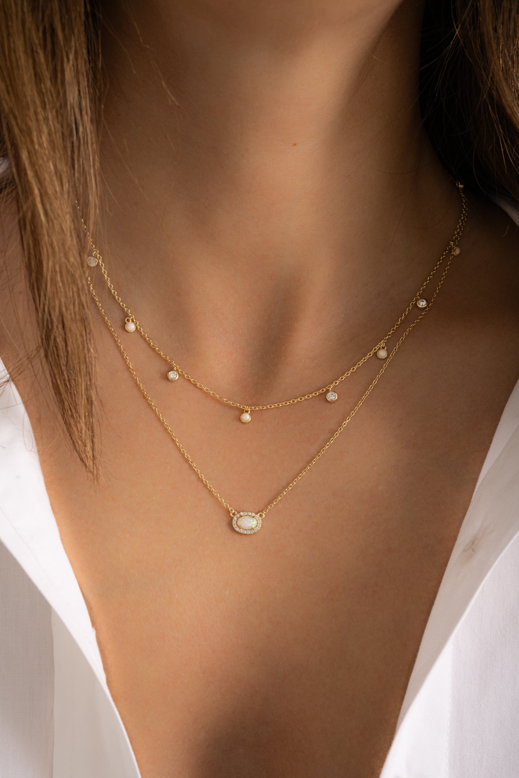 Model wearing dainty gold opal and cz charm necklace and opal oval halo pendant in a stack. 