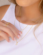 Model wearing three gold necklaces in a stack featuring dainty designs with cz stones. 