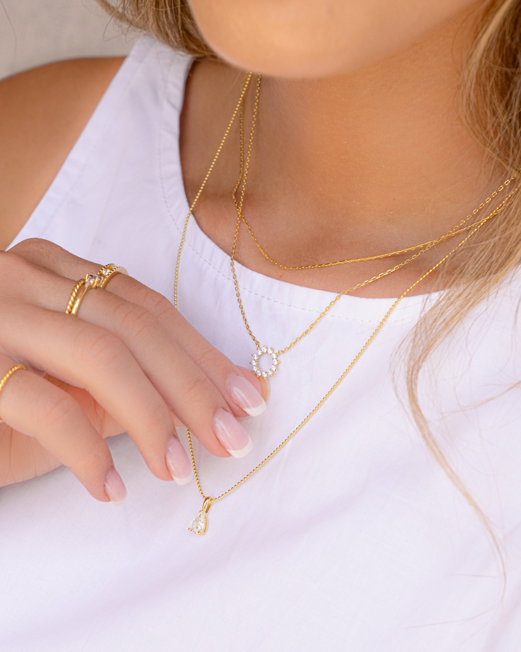 Model wearing three gold necklaces in a stack featuring dainty designs with cz stones. 