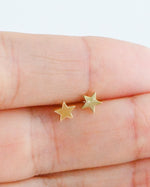 Model holding small plain gold star stud earrings. 
