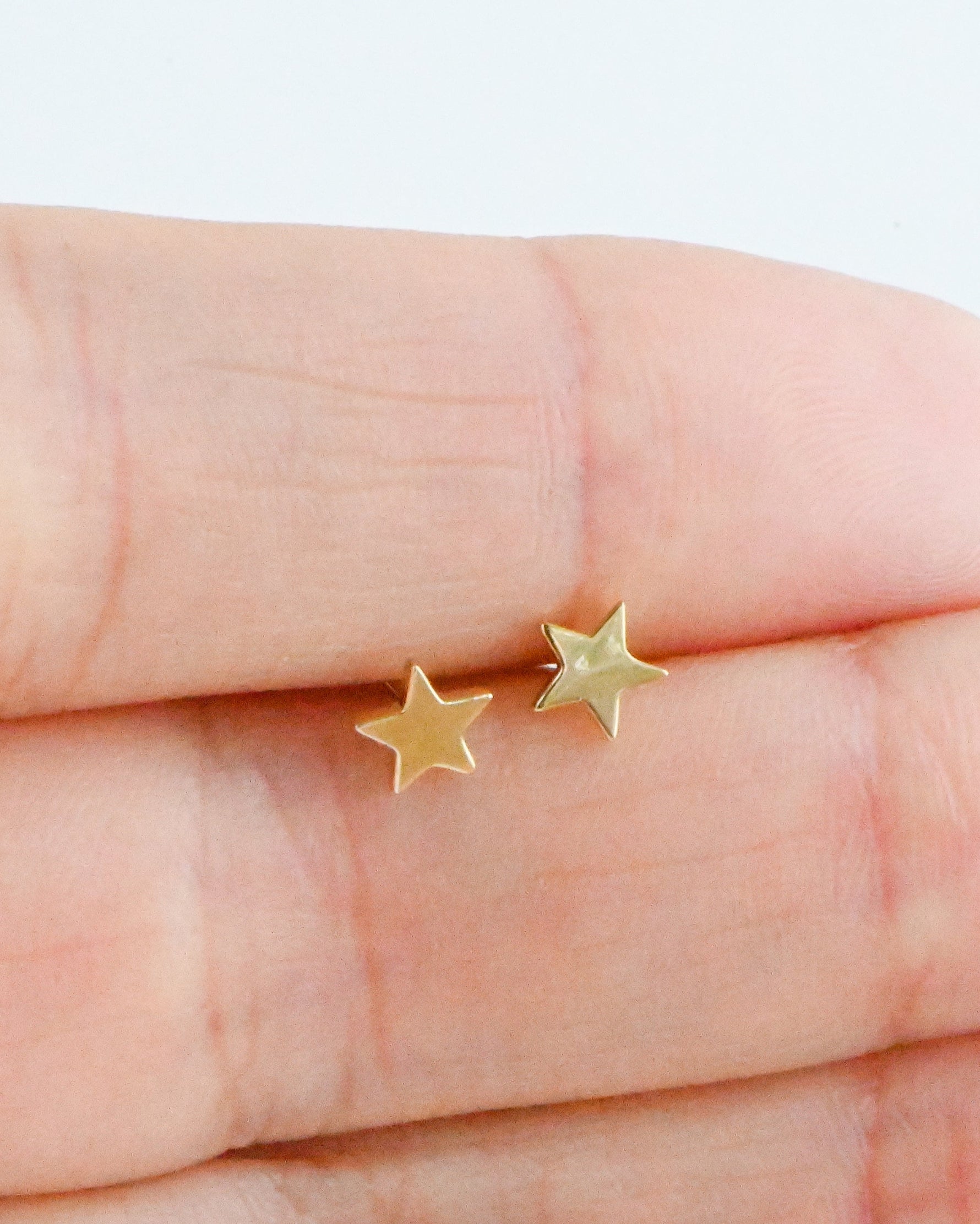 Model holding small plain gold star stud earrings. 