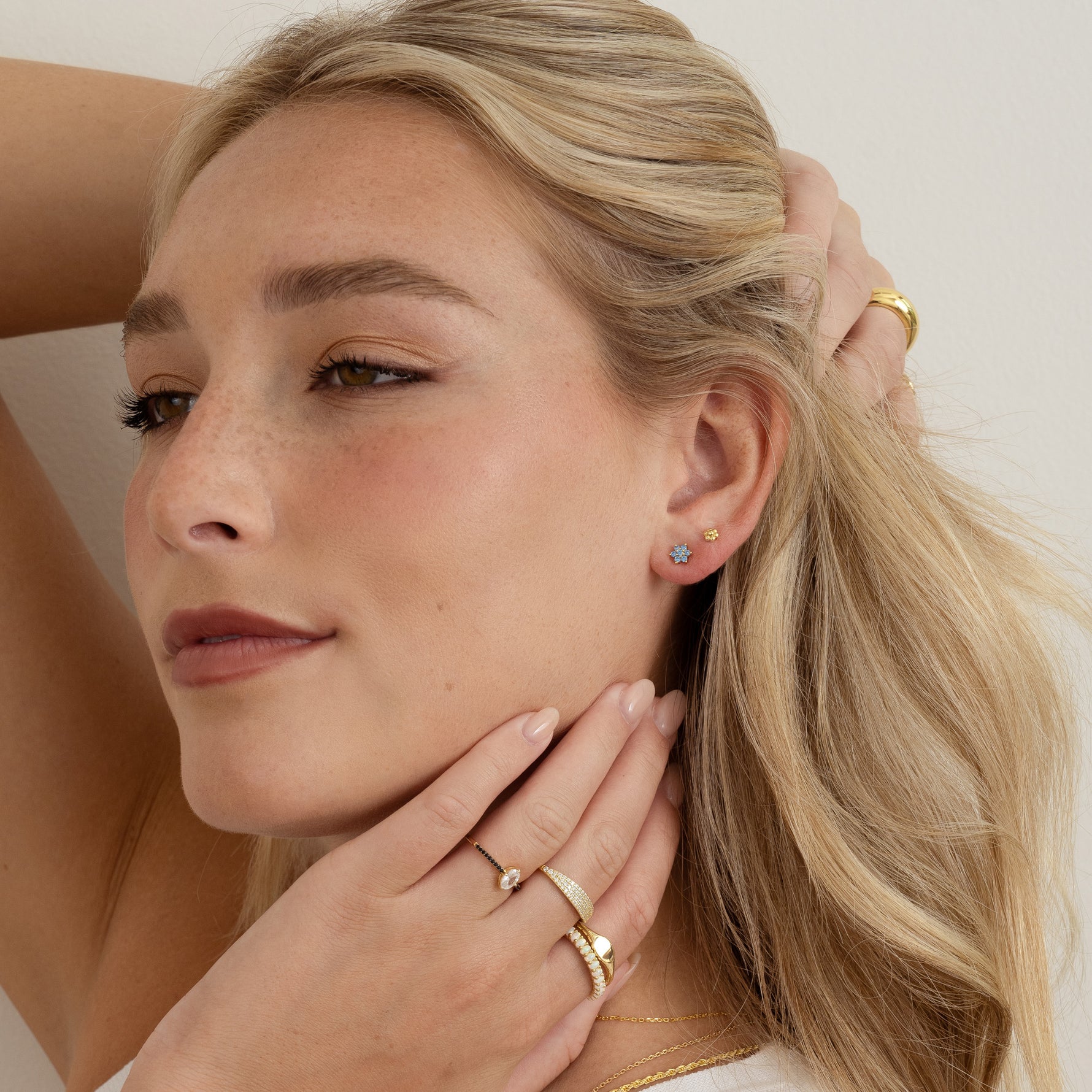 Model wearing dainty gold earring stack featuring an aqua flower stud and a gold flower stud, paired with gold stacking rings. 