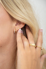 Model wearing dainty everyday gold earrings featuring a heart diamond bezel stud and gold stacking rings.