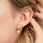 Model wearing fancy gold pearl drop huggie earrings.