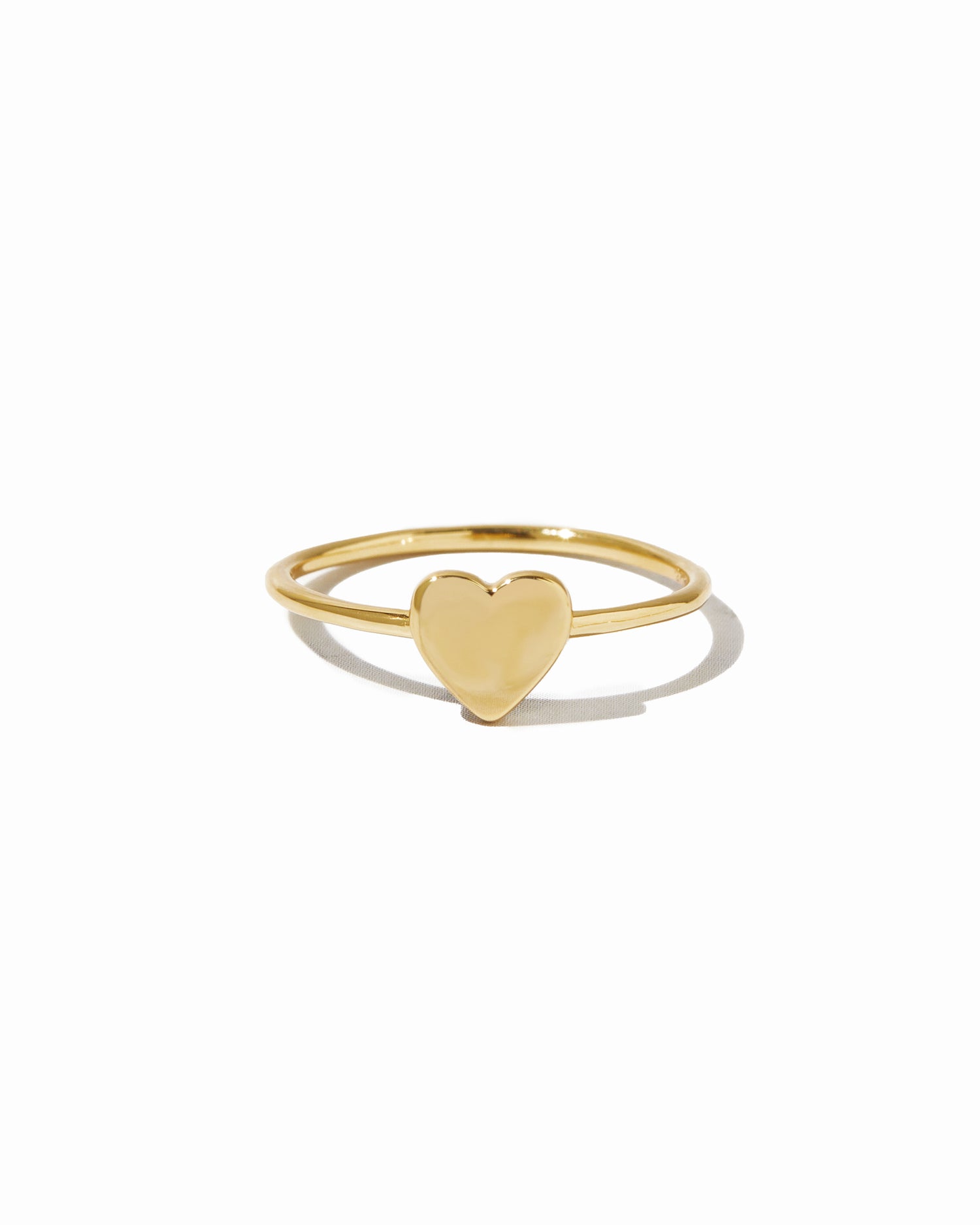 Plain solitaire gold heart ring on white background.