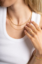 Model wearing gold paperclip chain necklace layered with a gold simple beaded chain necklace and gold stacking rings. 