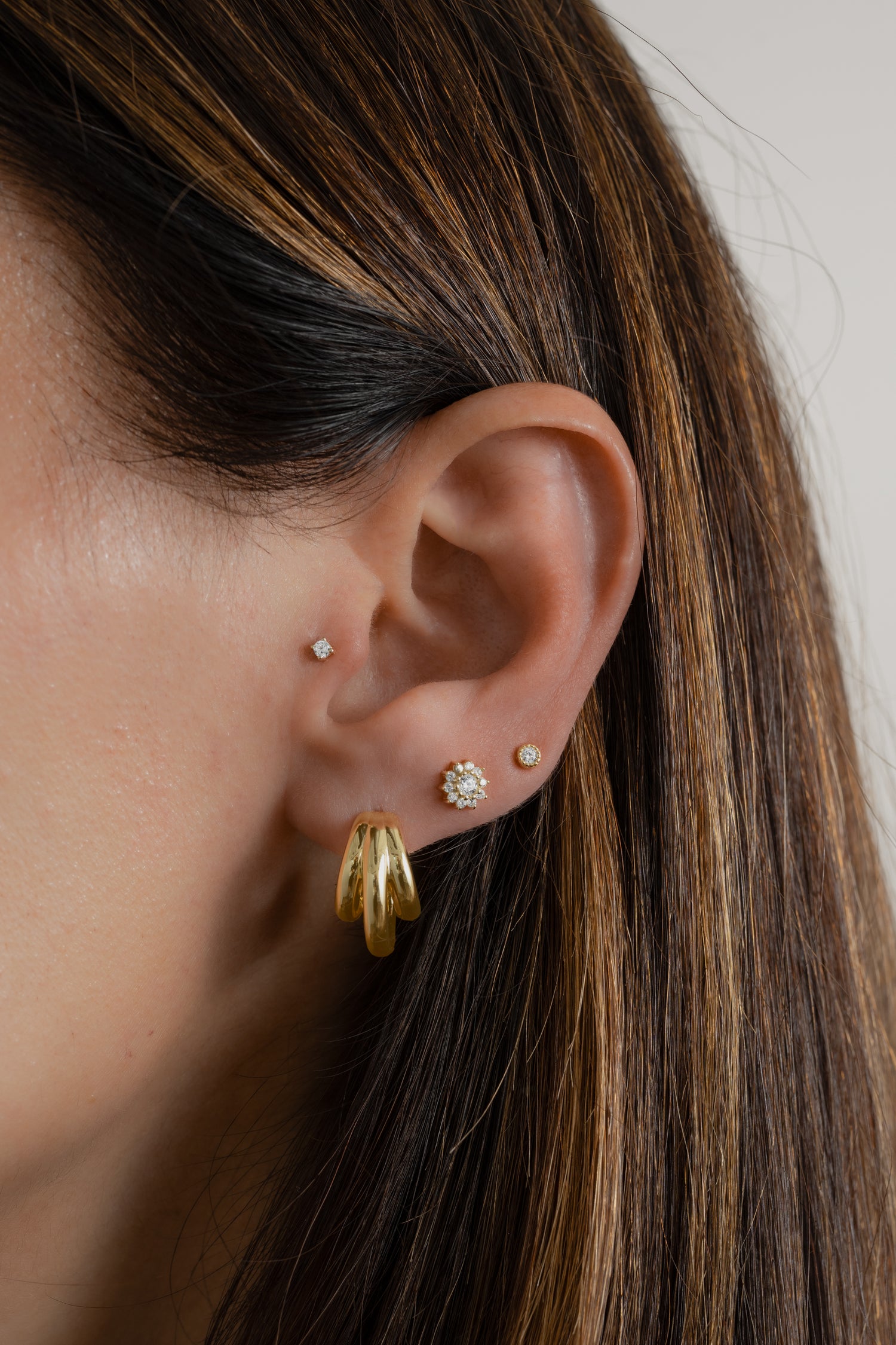 Model wearing gold triple hoop earrings with dainty diamond flower stud earrings and bezel diamond studs