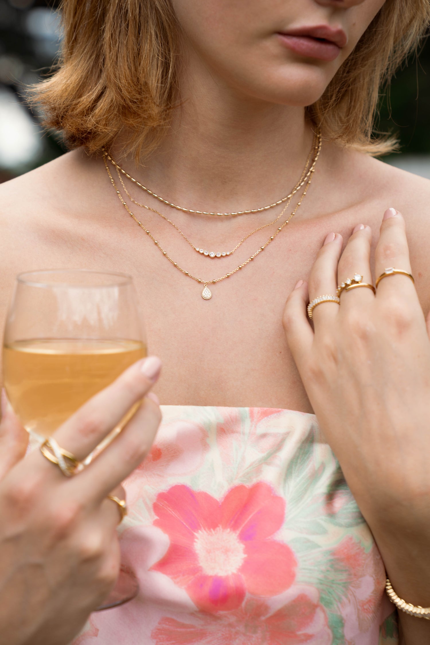 Model wearing three gold layered necklaces including a rice beaded necklace, a gradient bar necklace, and a beaded tear drop necklace. 