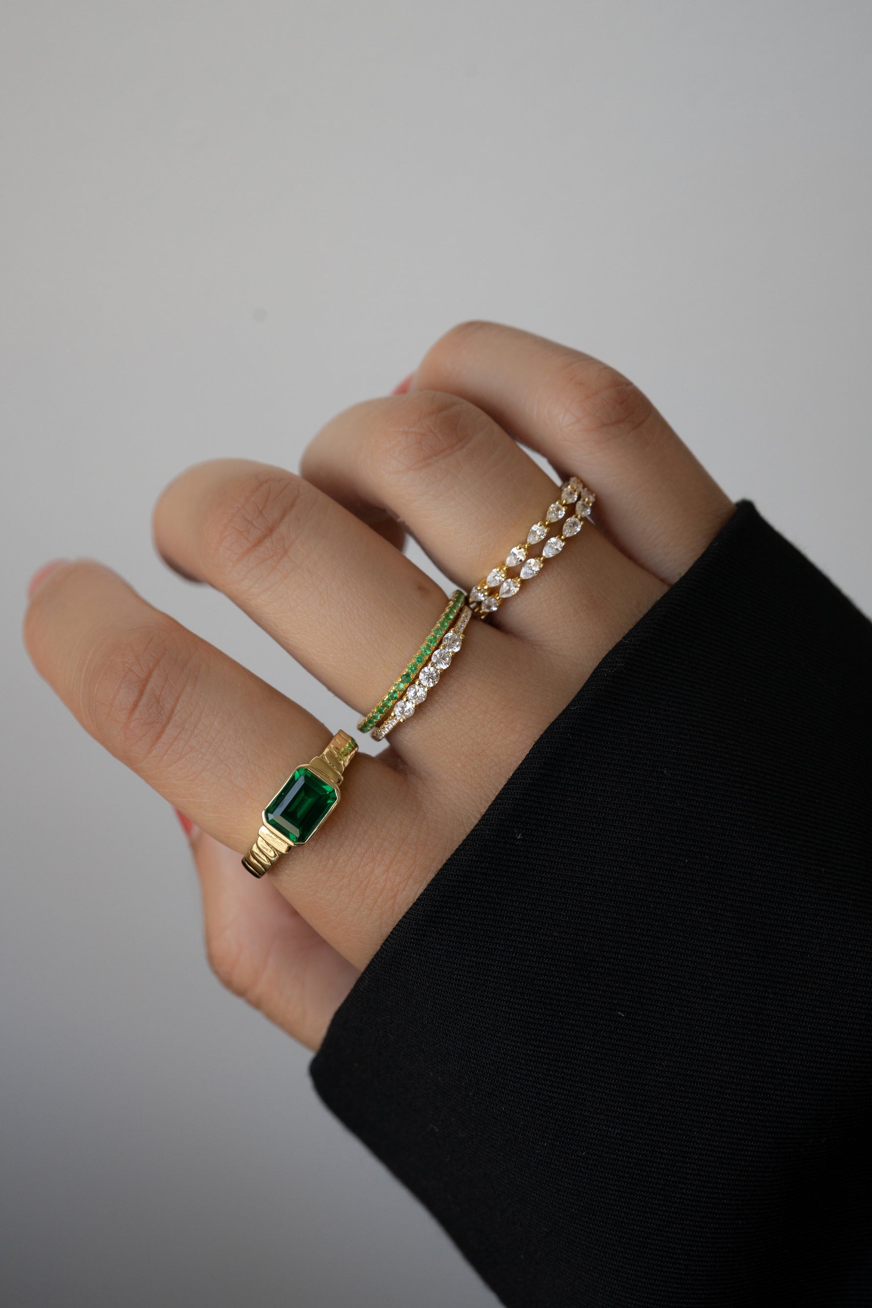 Model wearing gold emerald and diamond ring stack for a bold look. 
