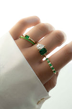 Model wearing statement emerald birthstone ring stack including a toi et moi ring, a simple baguette emerald ring, a cz eternity ring, and a statement emerald and cz alternating ring. 