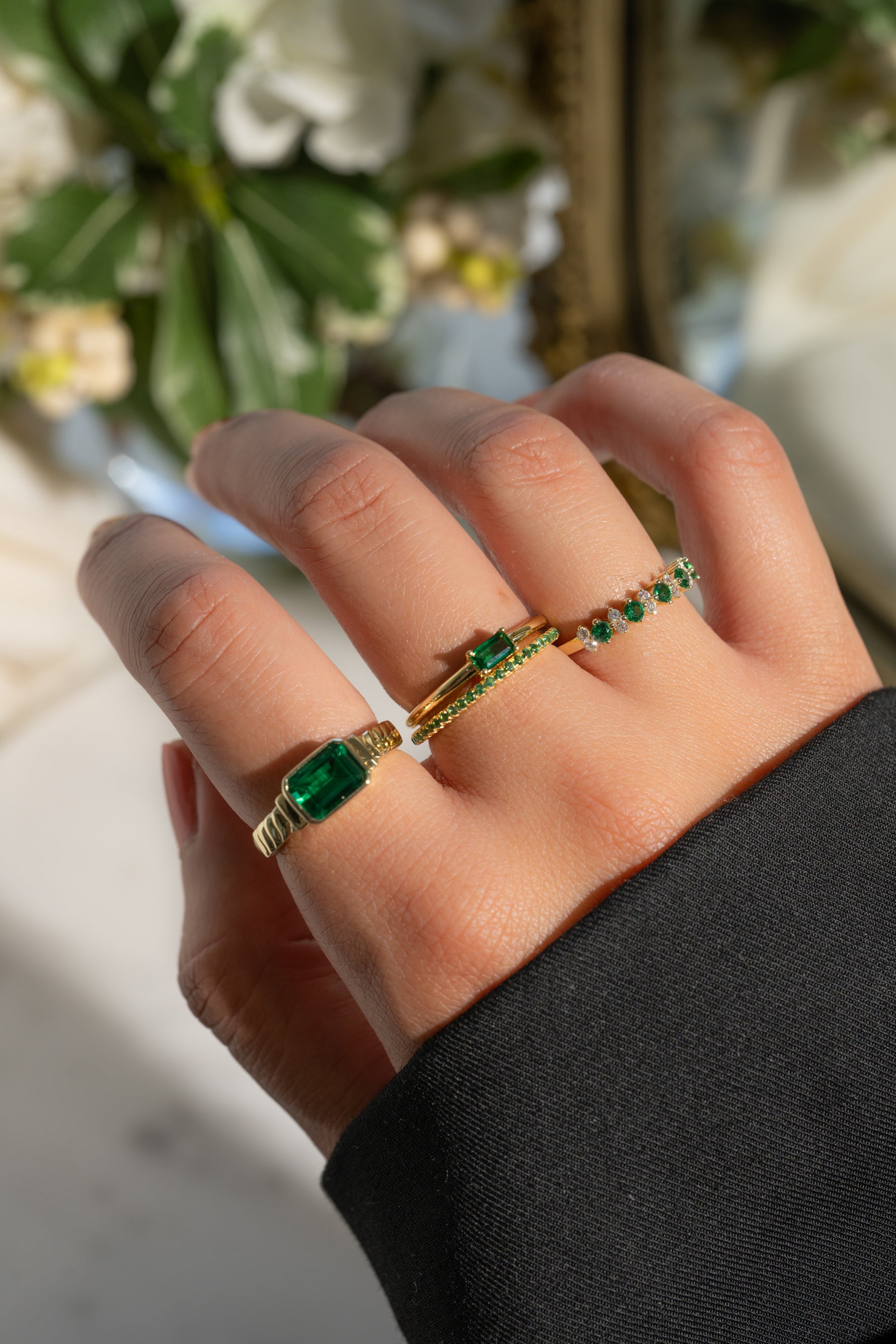 Model wearing emerald birthstone rings in a stack. 