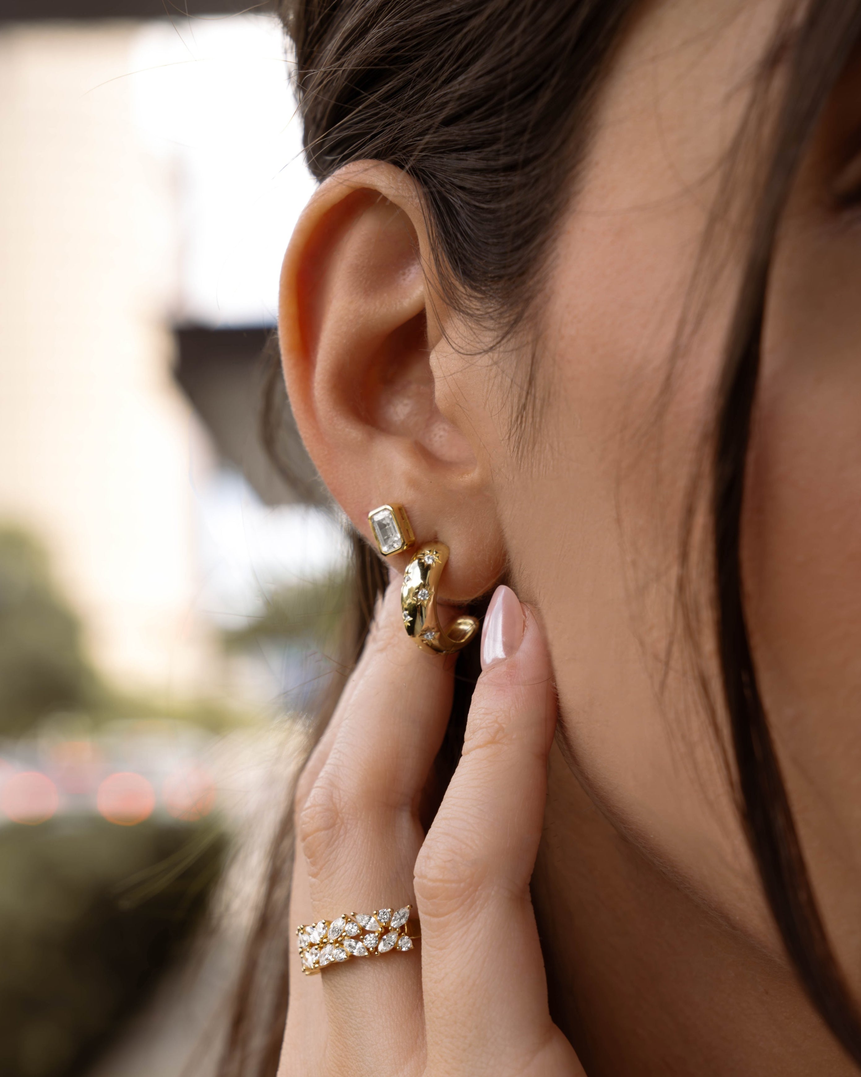Model wearing fancy gold emerald cut stud earrings in her second hole and starburst dome hoop earrings in her first hole. 