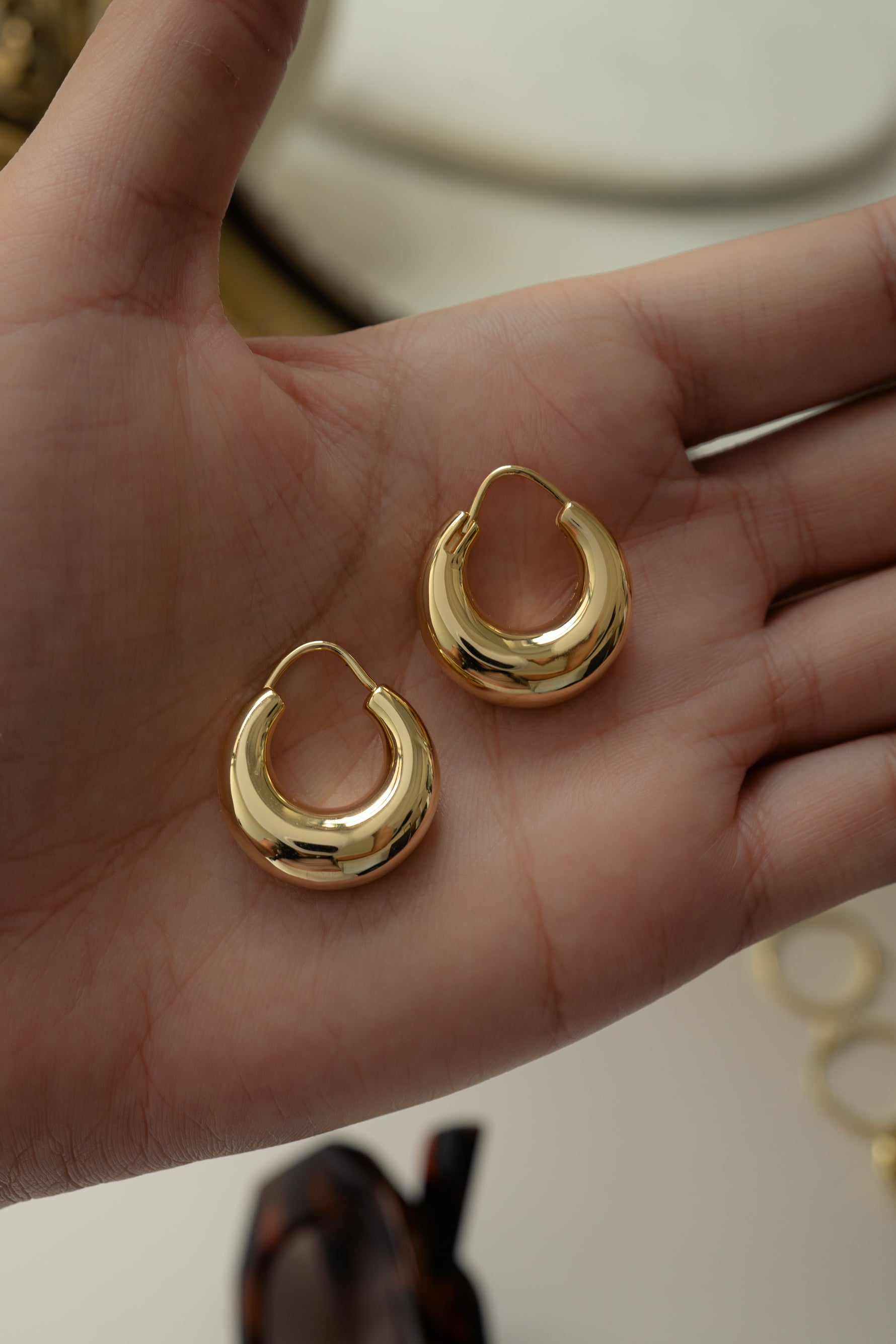 Model holding lightweight gold basket chunky hoop earrings in the palm of their hand.