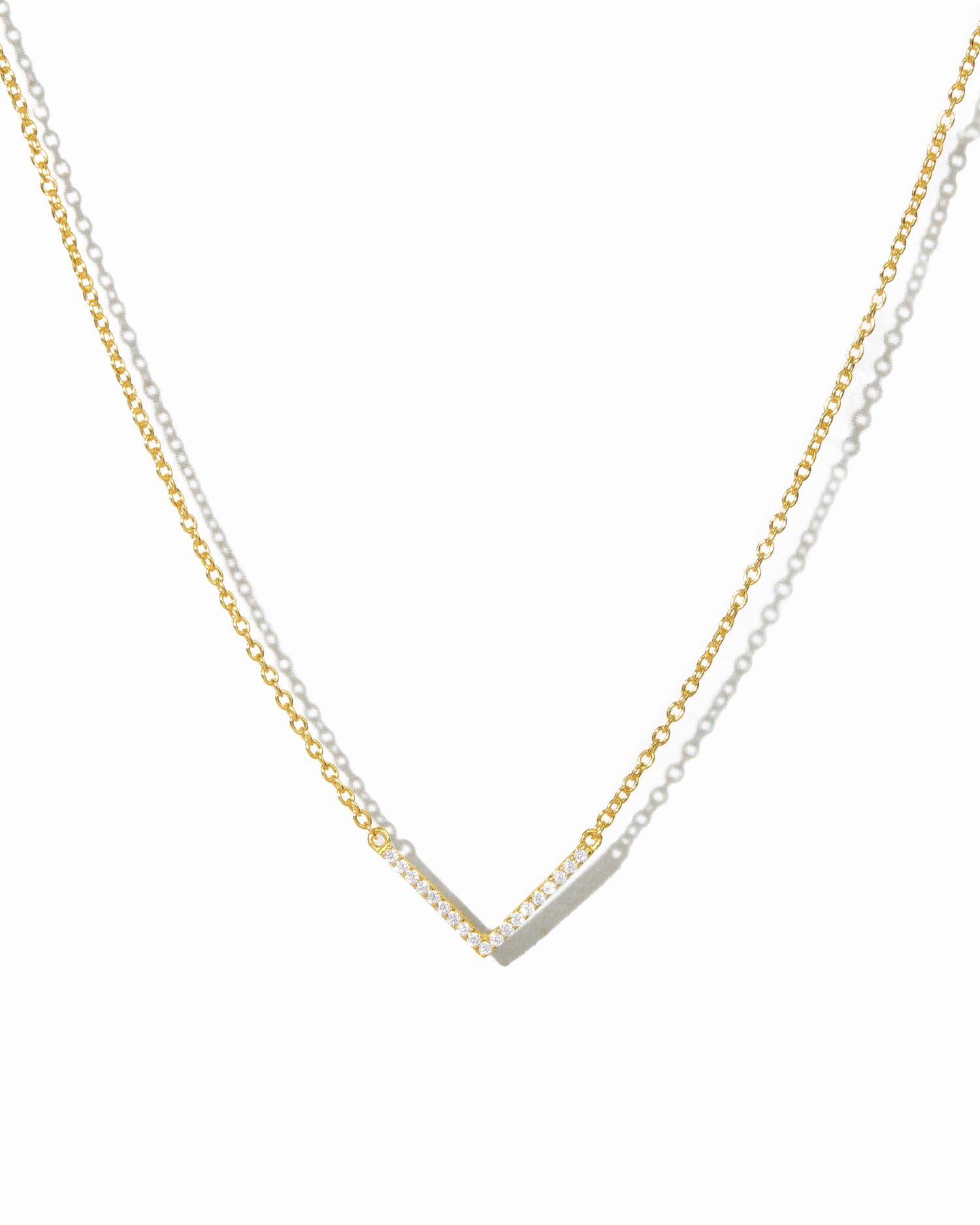 delicate gold chevron necklace on white background.