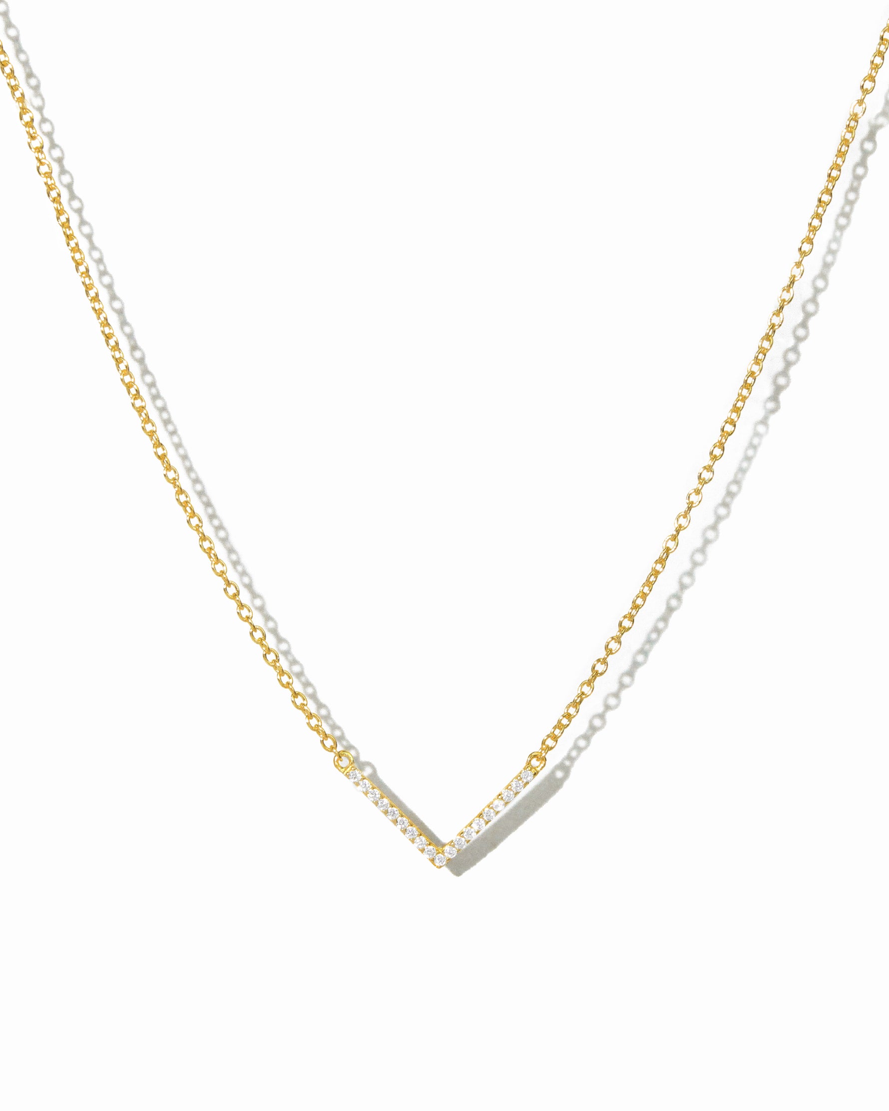 delicate gold chevron necklace on white background.