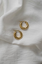 Sleek gold chunky hoop earrings on white soft fabric. 