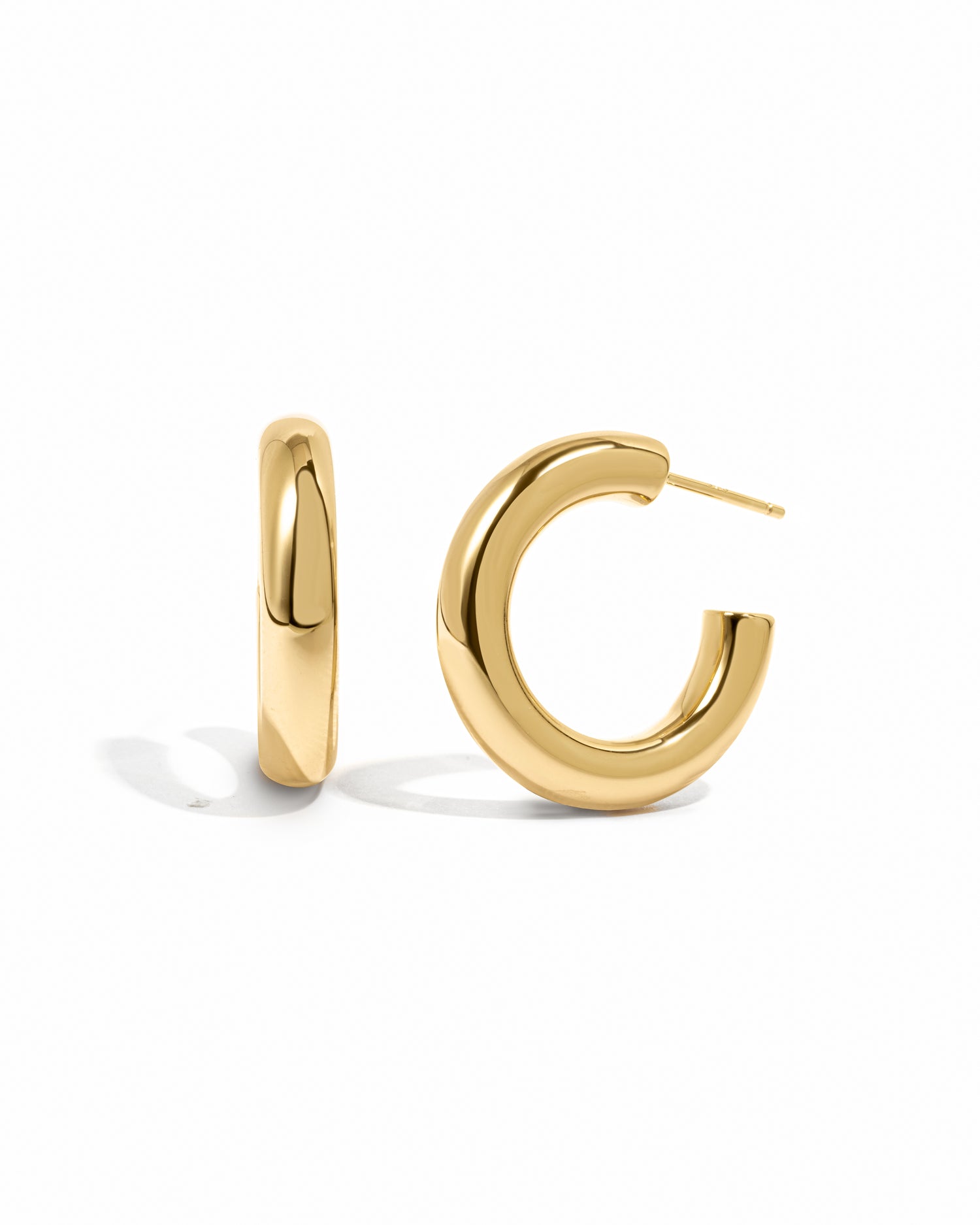 Sleek chunky gold tube hoop earrings on white background