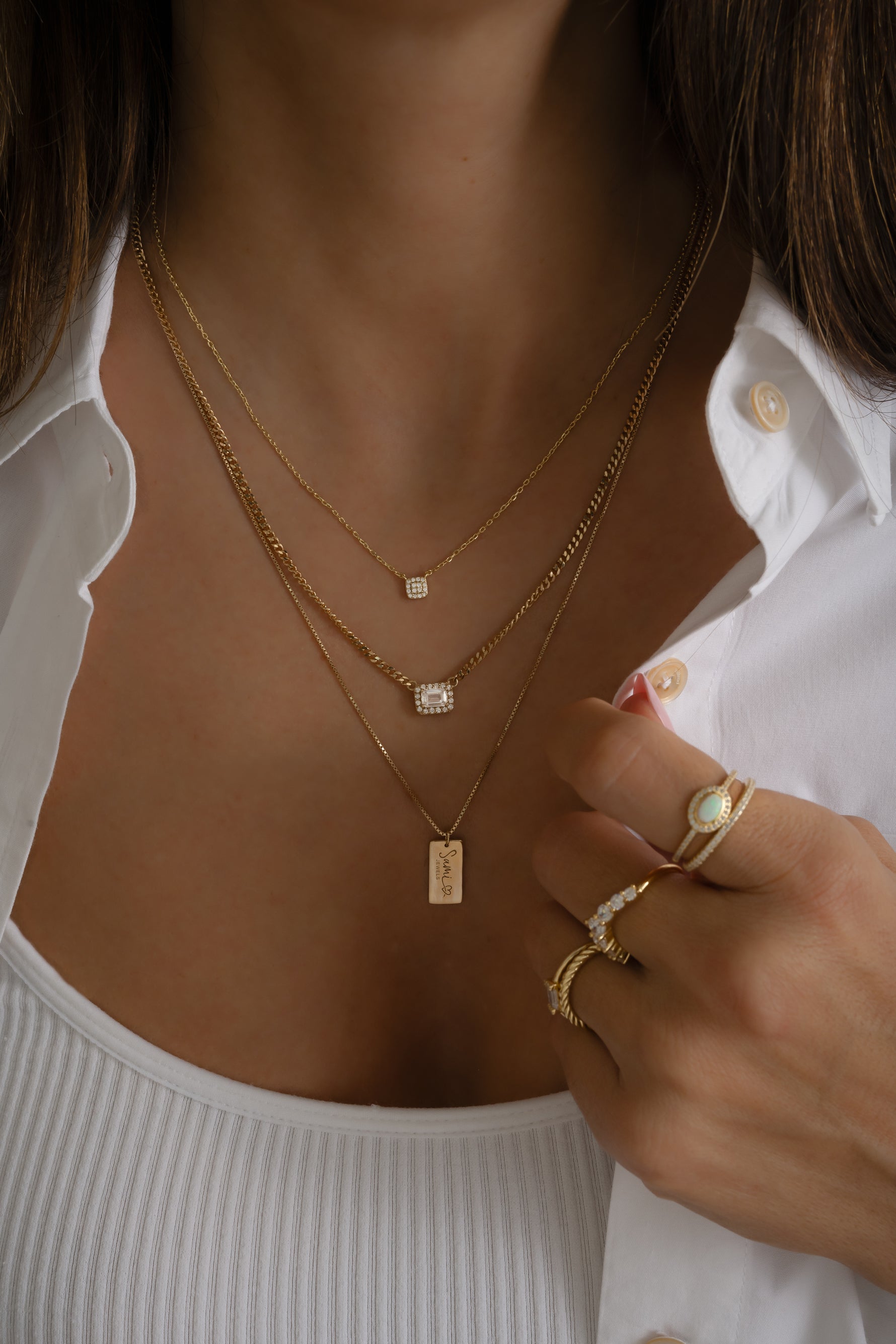 Model wearing dainty gold custom dog tag name necklace in a stack with a baguette halo necklace and a tiny square cz necklace.