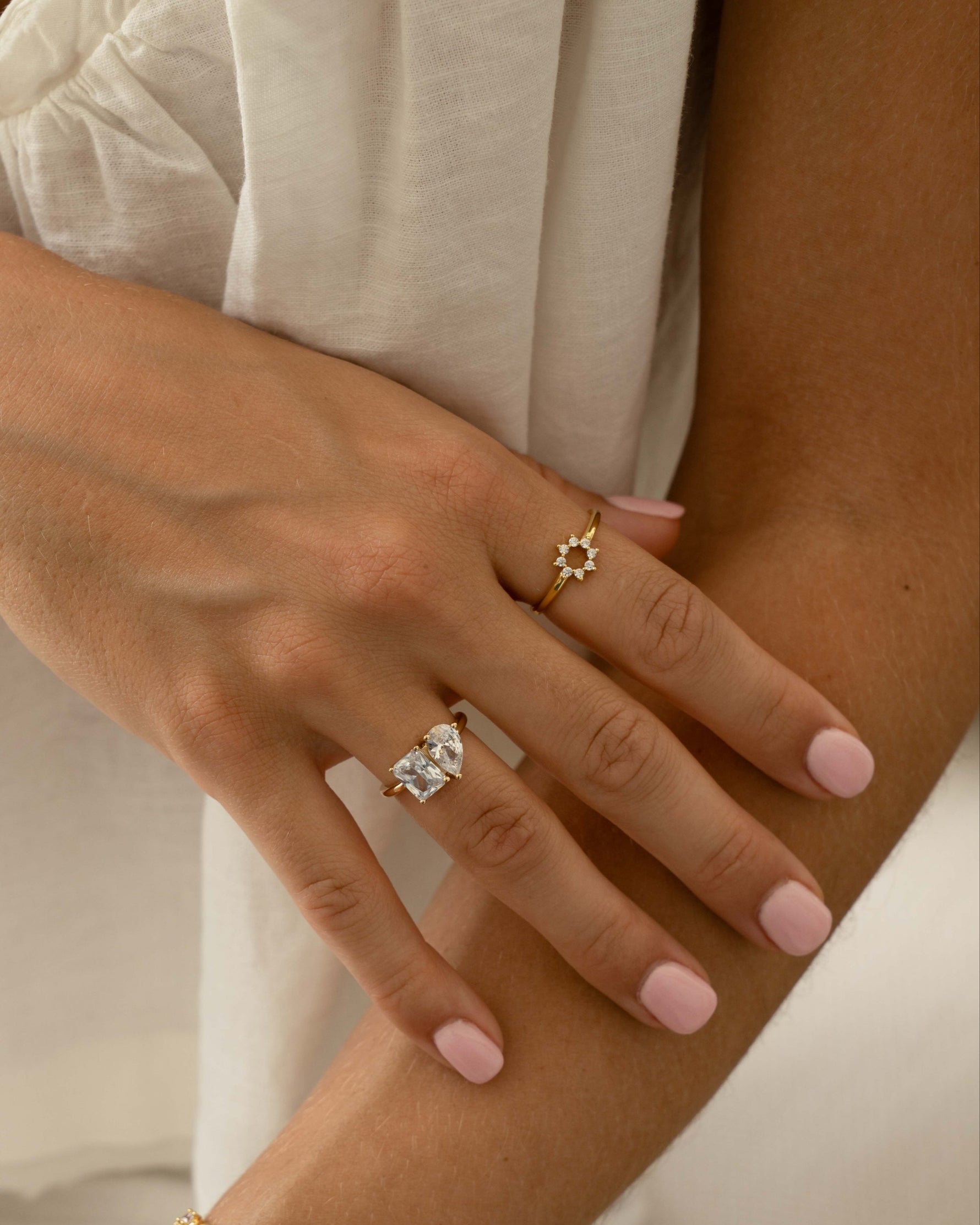 Model wearing a feminine gold ring stack featuring a sunburst ring with cz stones and a toi et moi statement engagement style ring. 