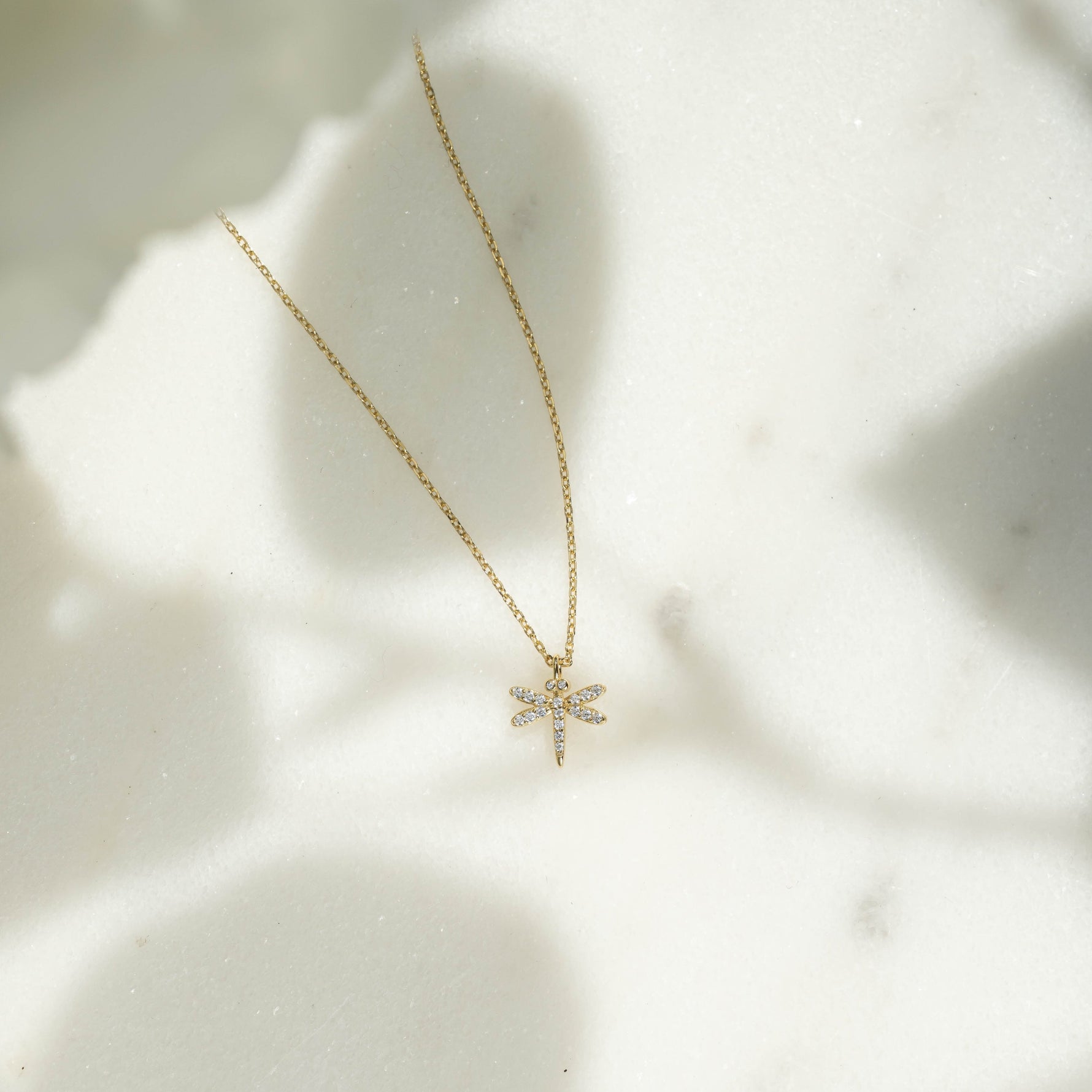 Flat lay of dainty gold dragonfly pendant necklace. 