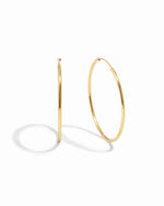 Thin oversized infinity gold hoops on white background.