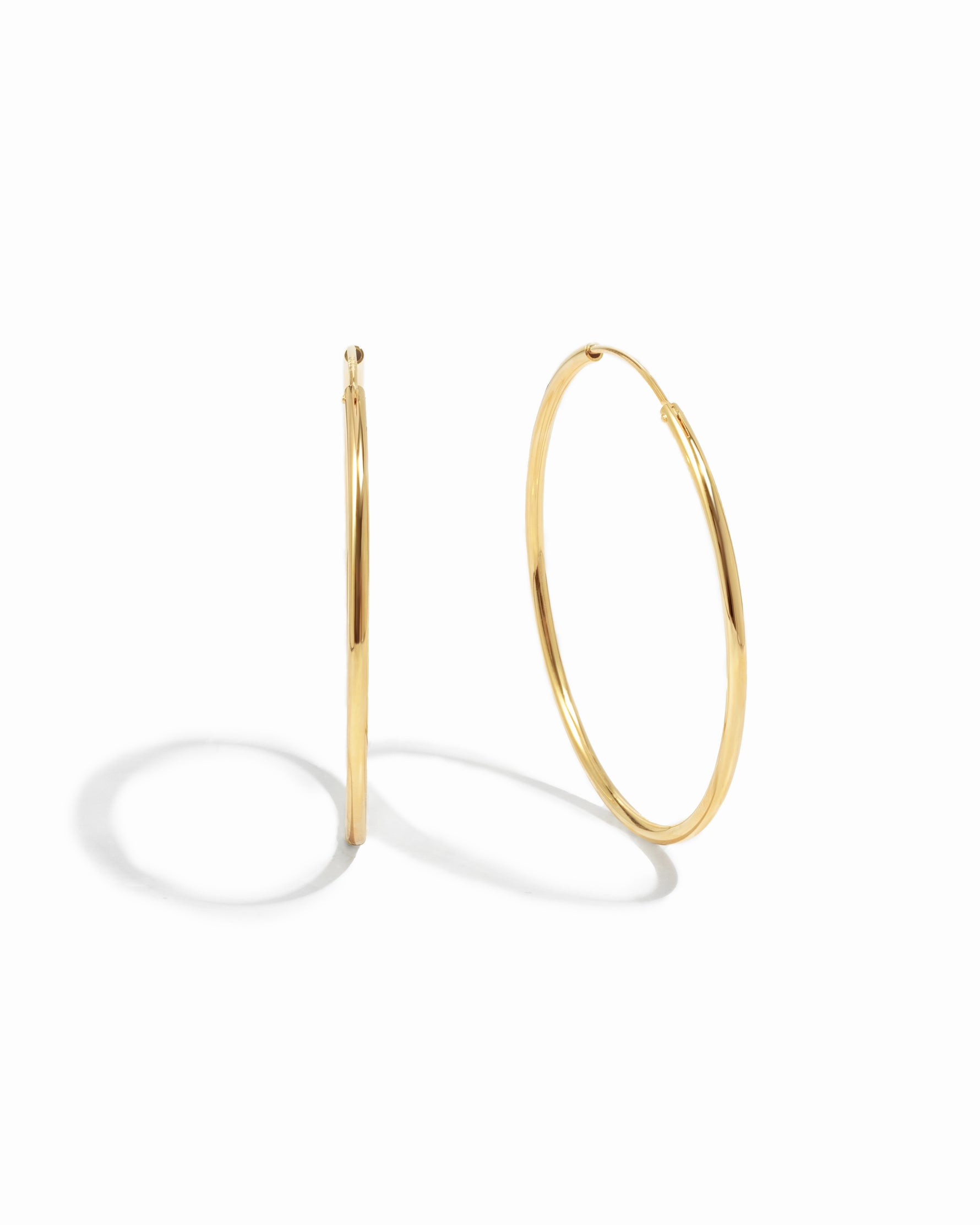 Thin oversized infinity gold hoops on white background.
