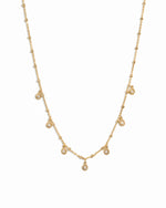 Dangling gold tear drop beaded chain necklace on white background.