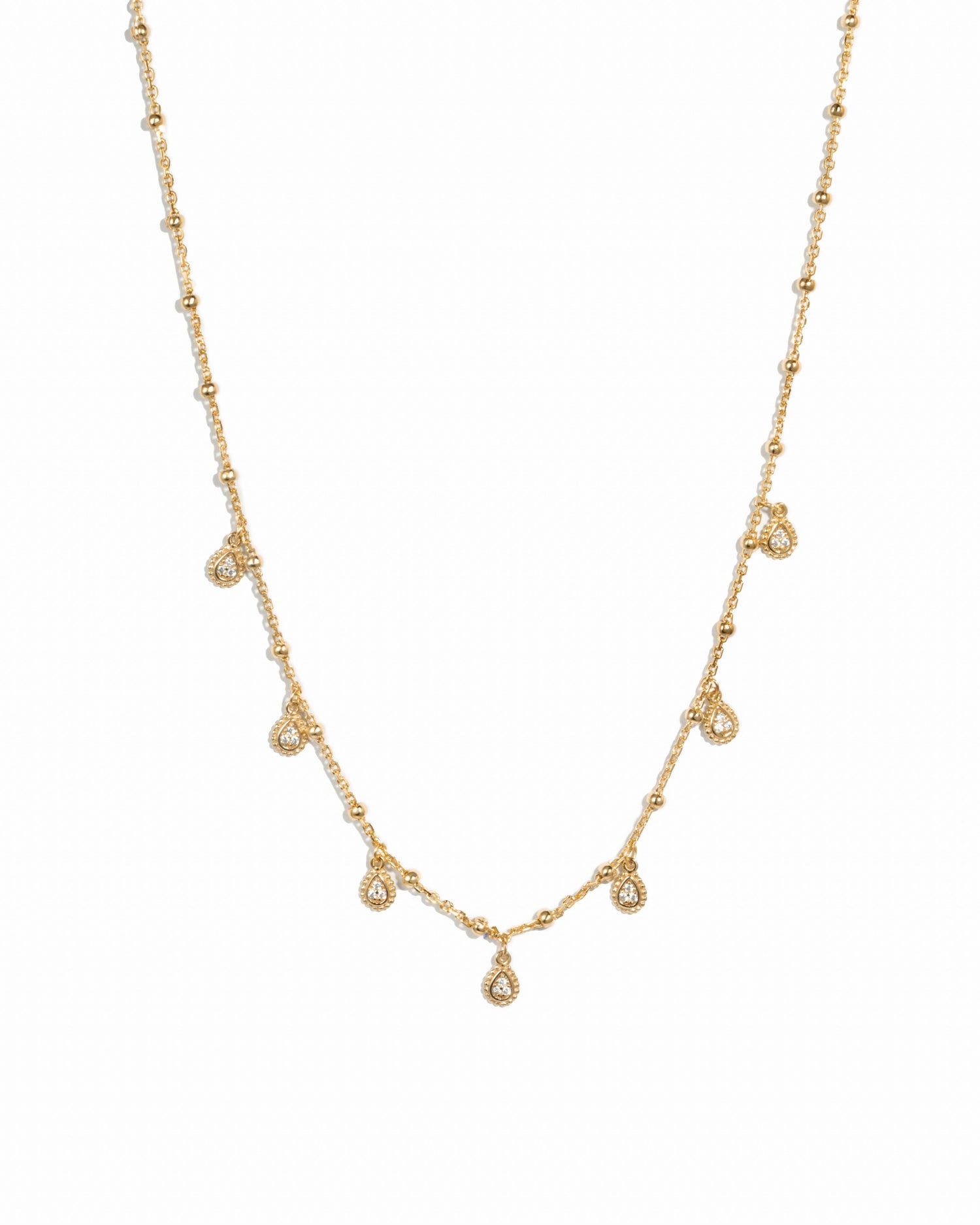 Dangling gold tear drop beaded chain necklace on white background.