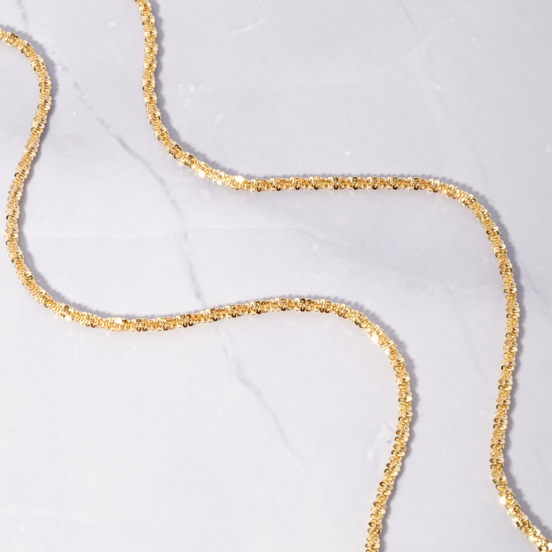 Sparkly gold diamond cut chain necklace on marble background.