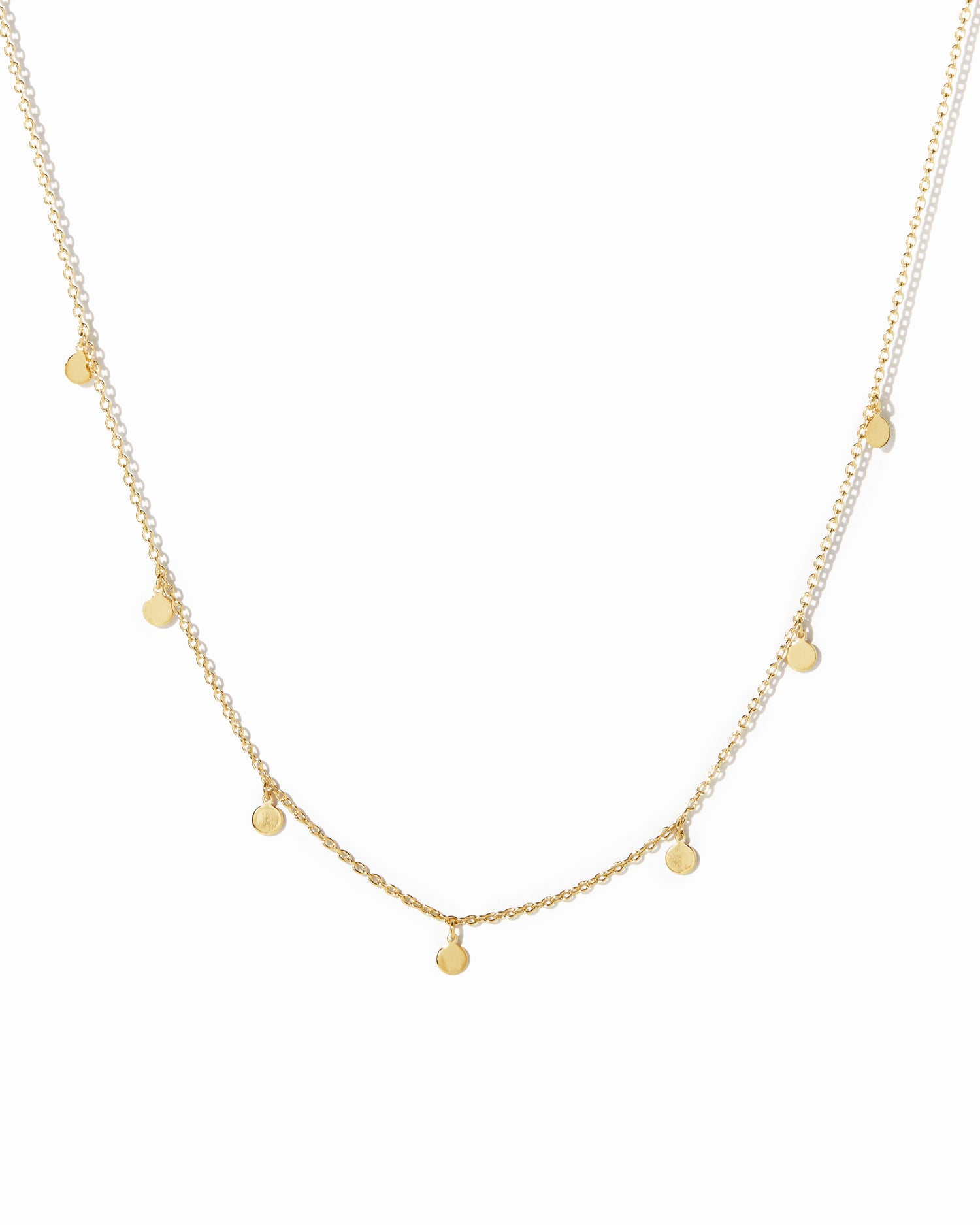 Dainty gold disc charm necklace on white background.
