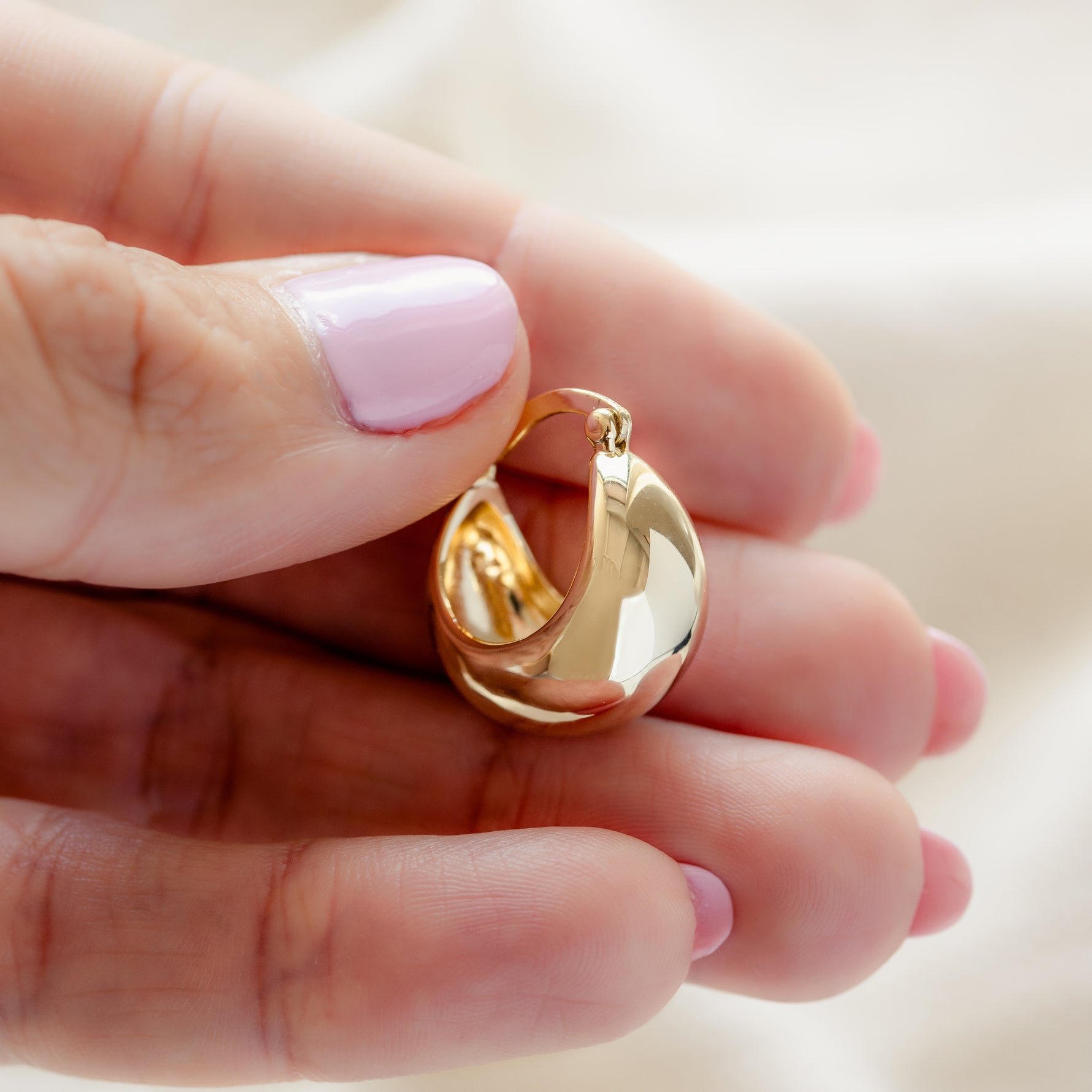 Model holding trendy gold basket tube hoop earrings. 